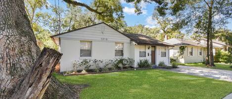 A single-story house with a number 1210 on the front, surrounded by a well-maintained lawn and trees.