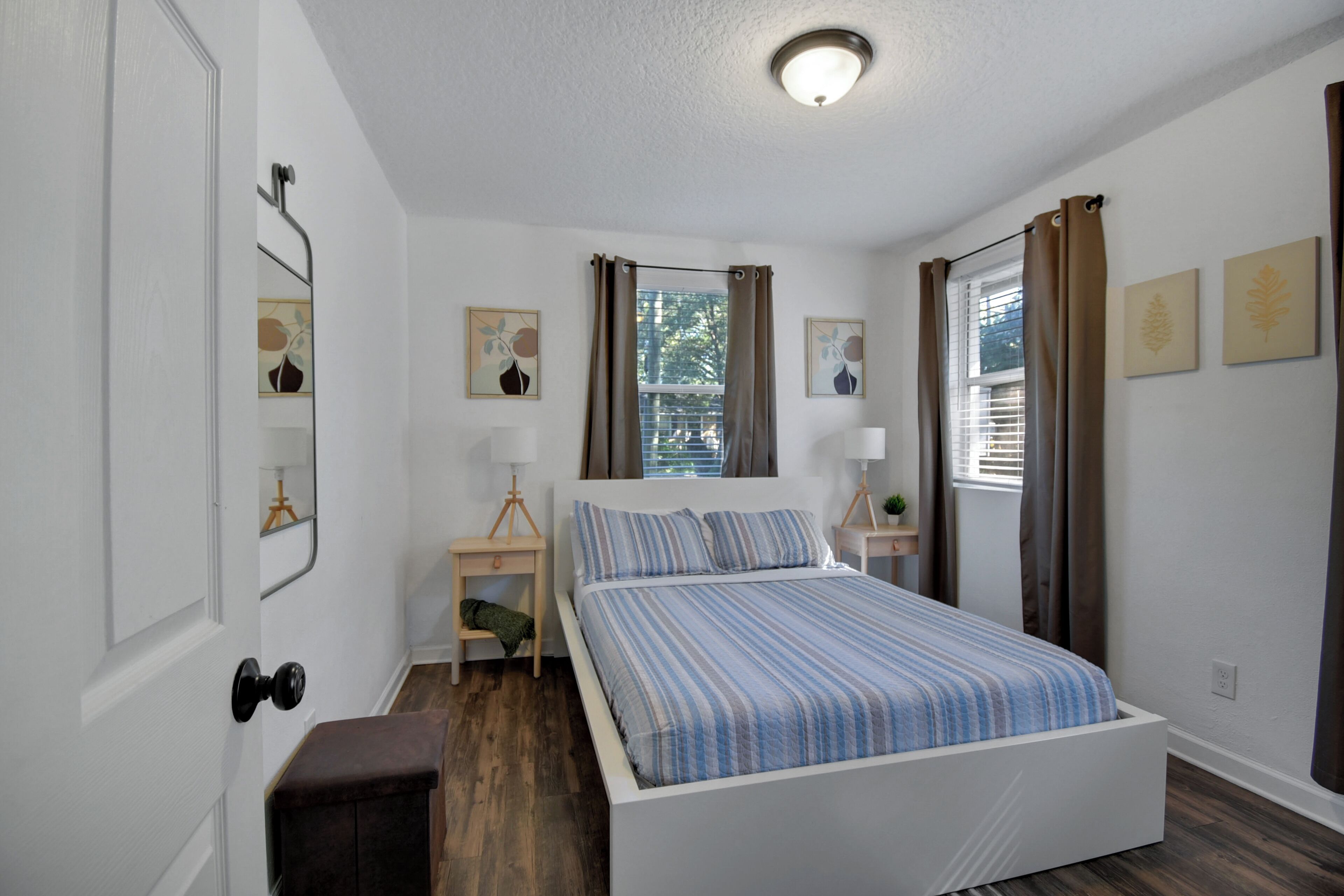 A bedroom with a bed, bedside tables, a window with curtains, and wall art.