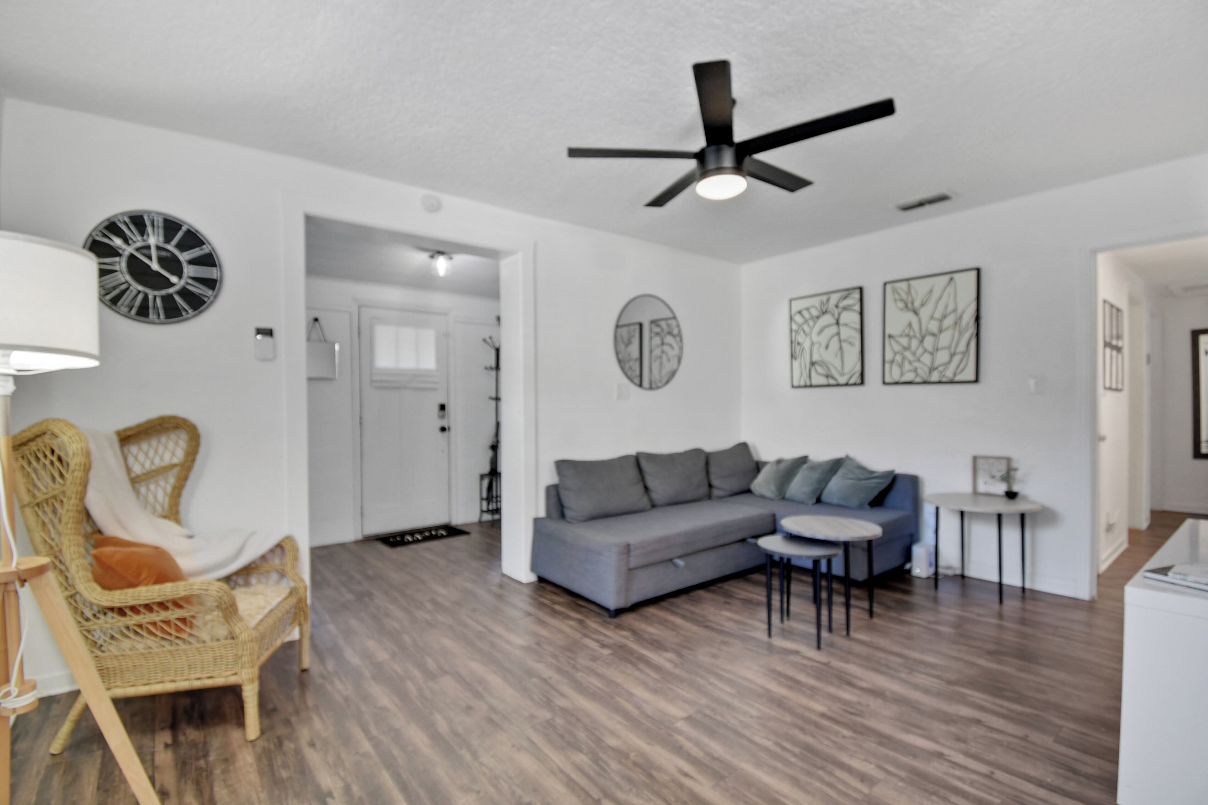 A modern living room with a grey sofa, a wicker chair, a small round table, and a ceiling fan.