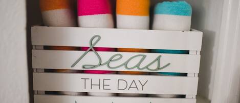 A white crate labeled "Seas The Day" with colorful towels inside.