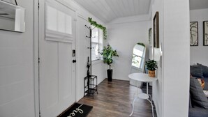 A hallway with a wooden floor, white walls, a coat rack, a potted plant, a small table, and a door with a doormat. - Downtown Jacksonville Retreat Pet-friendly With Hot Tub & Backyard Oasis (Jacksonville)
