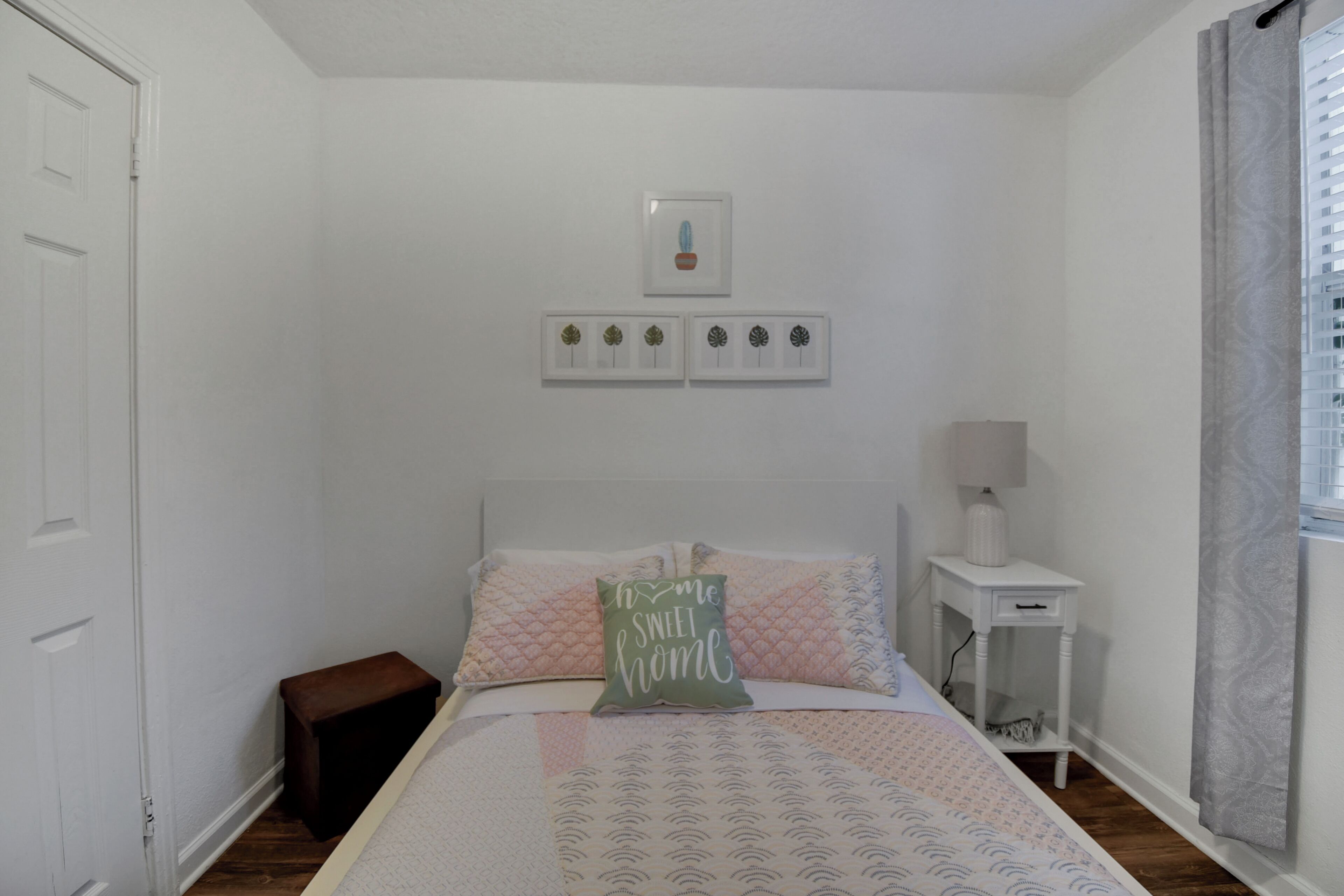 Un dormitori amb un llit, una taula de nit amb una làmpada, una petita estant i una finestra amb cortines.