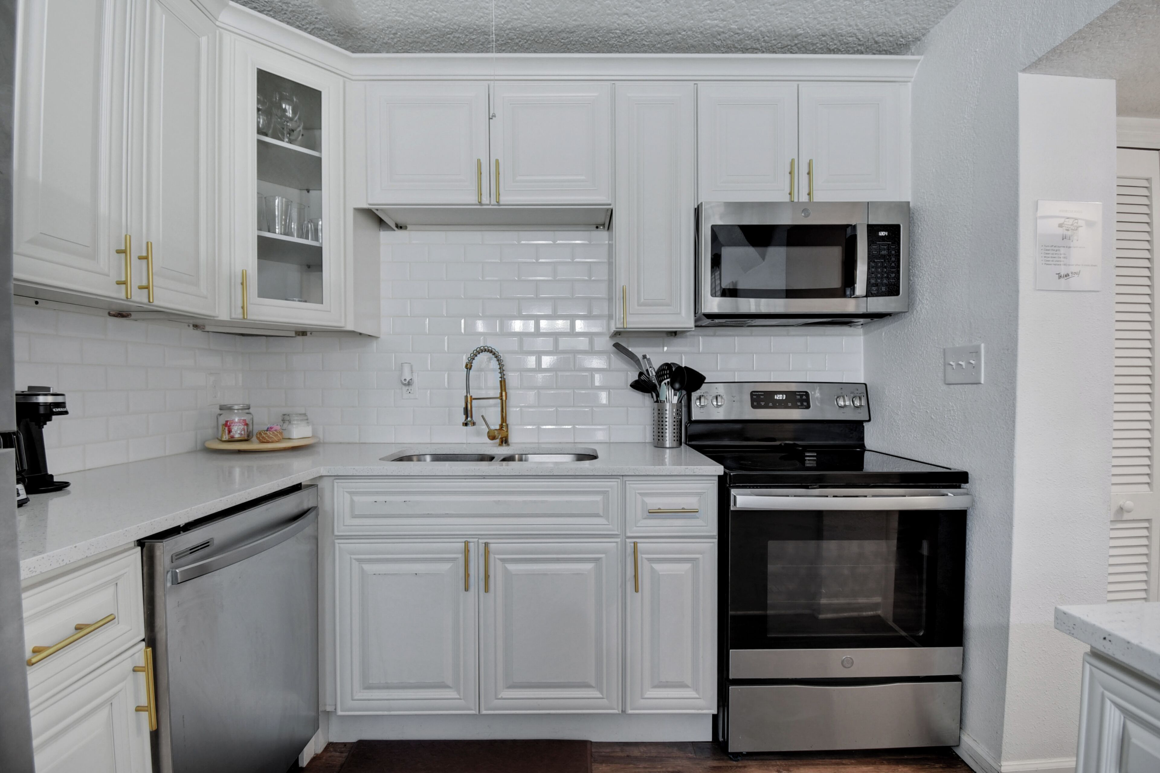 A modern kitchen with white cabinetry, a stainless steel dishwasher, a built-in oven, and a microwave.
