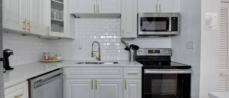 A modern kitchen with white cabinetry, a stainless steel dishwasher, a built-in oven, and a microwave.