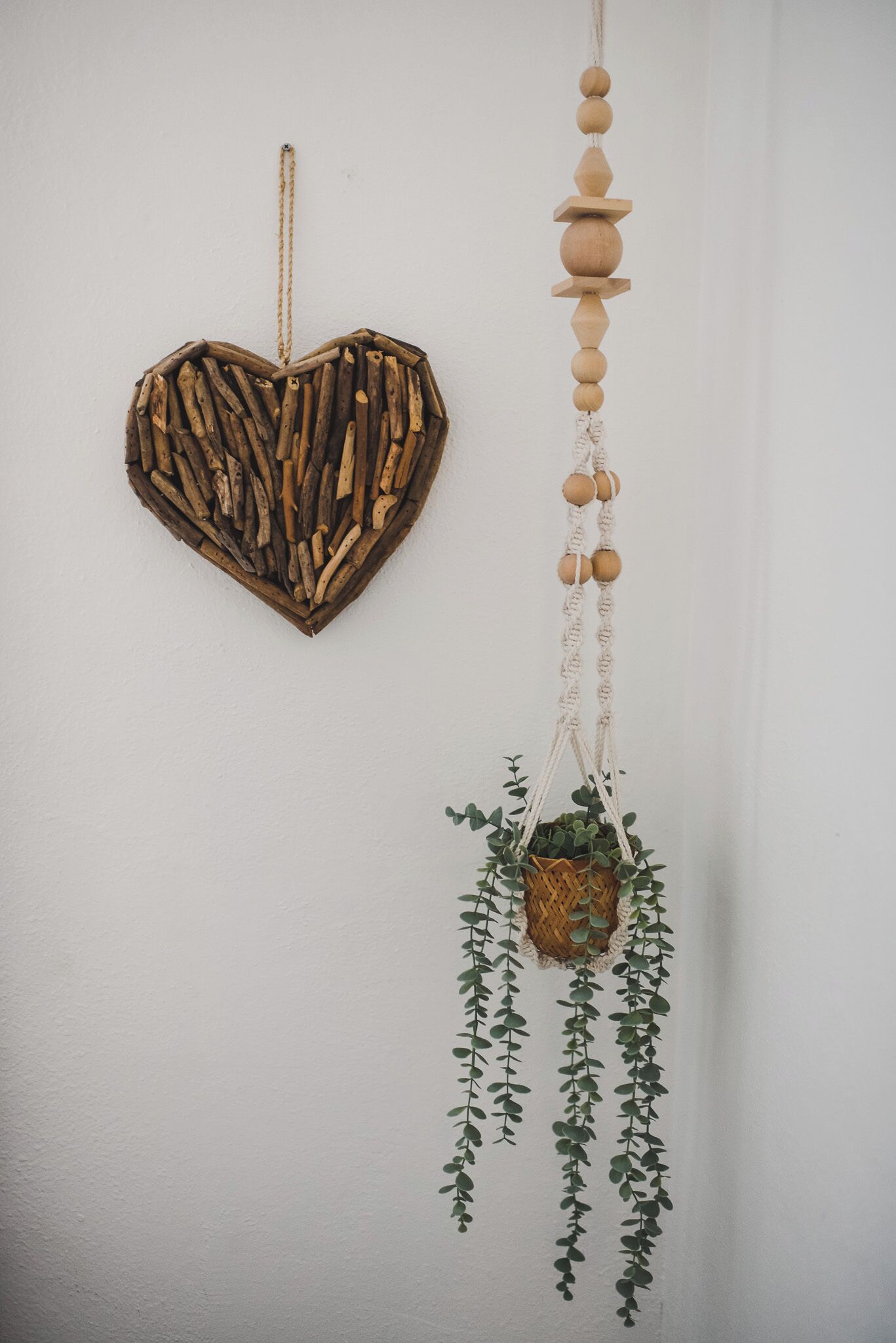 A wall with a heart-shaped wooden decoration and a macramé hanging with a plant.