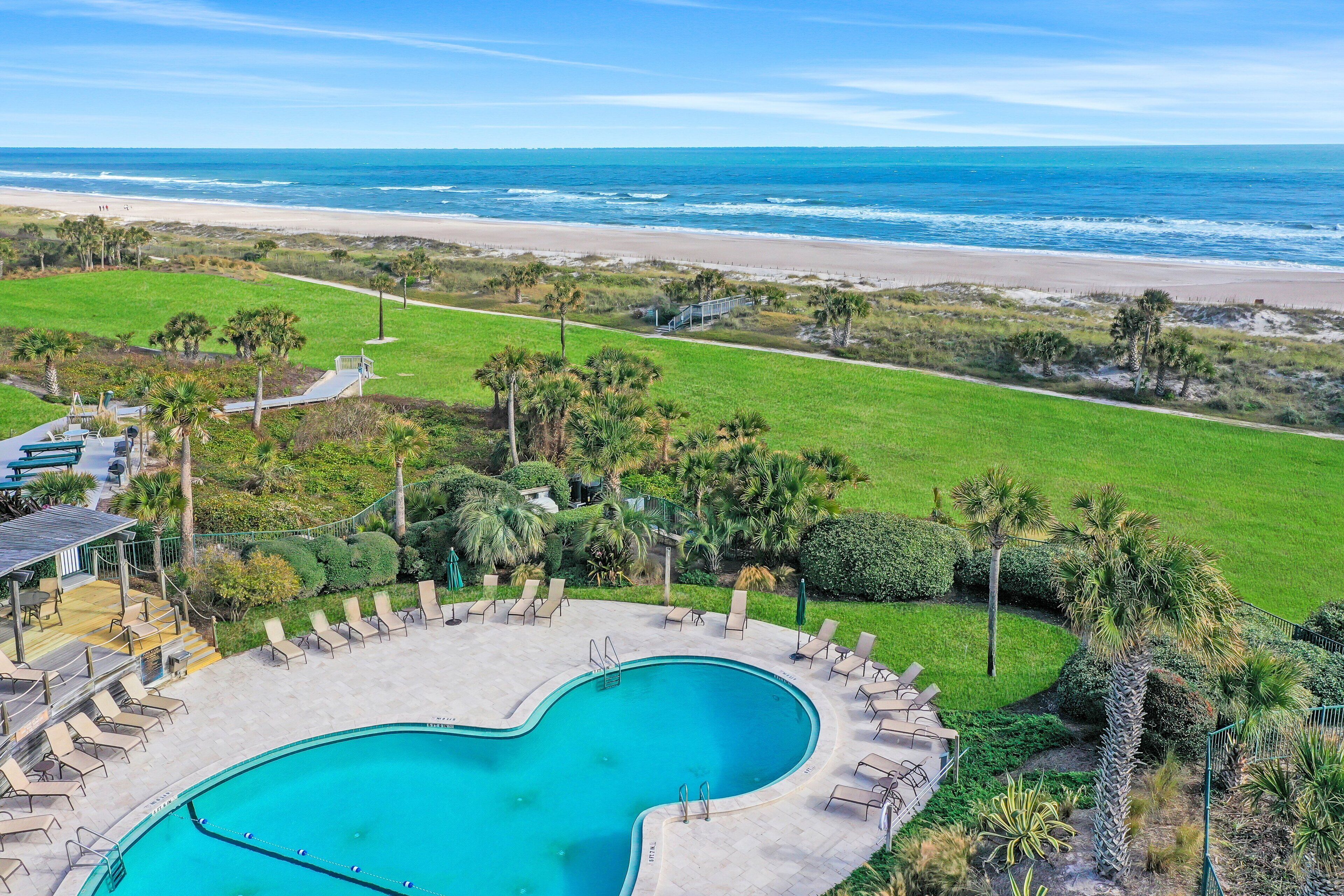 A swimming pool with lounge chairs and a view of the beach.