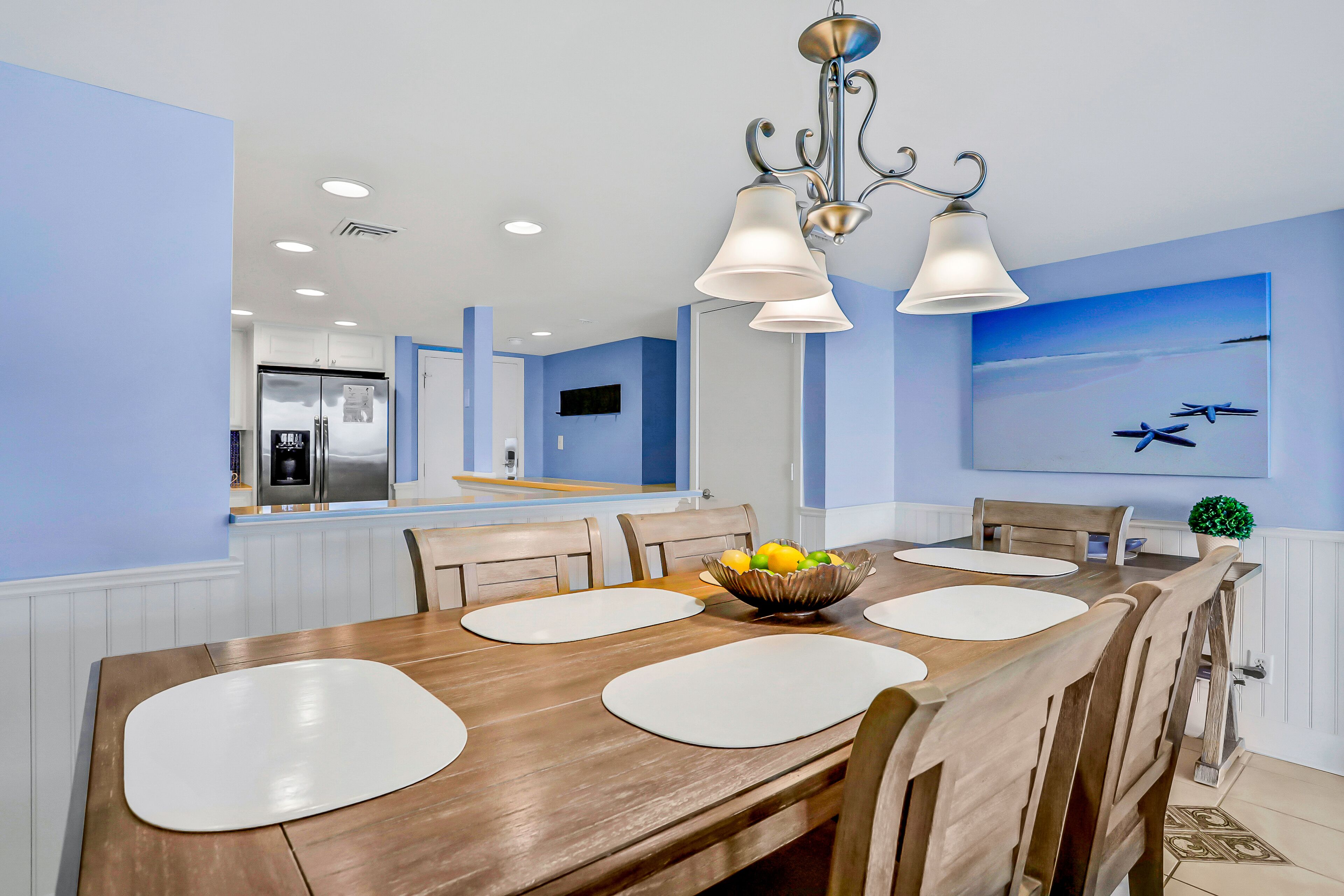 A dining area with a wooden table, white placemats, and a fruit bowl.