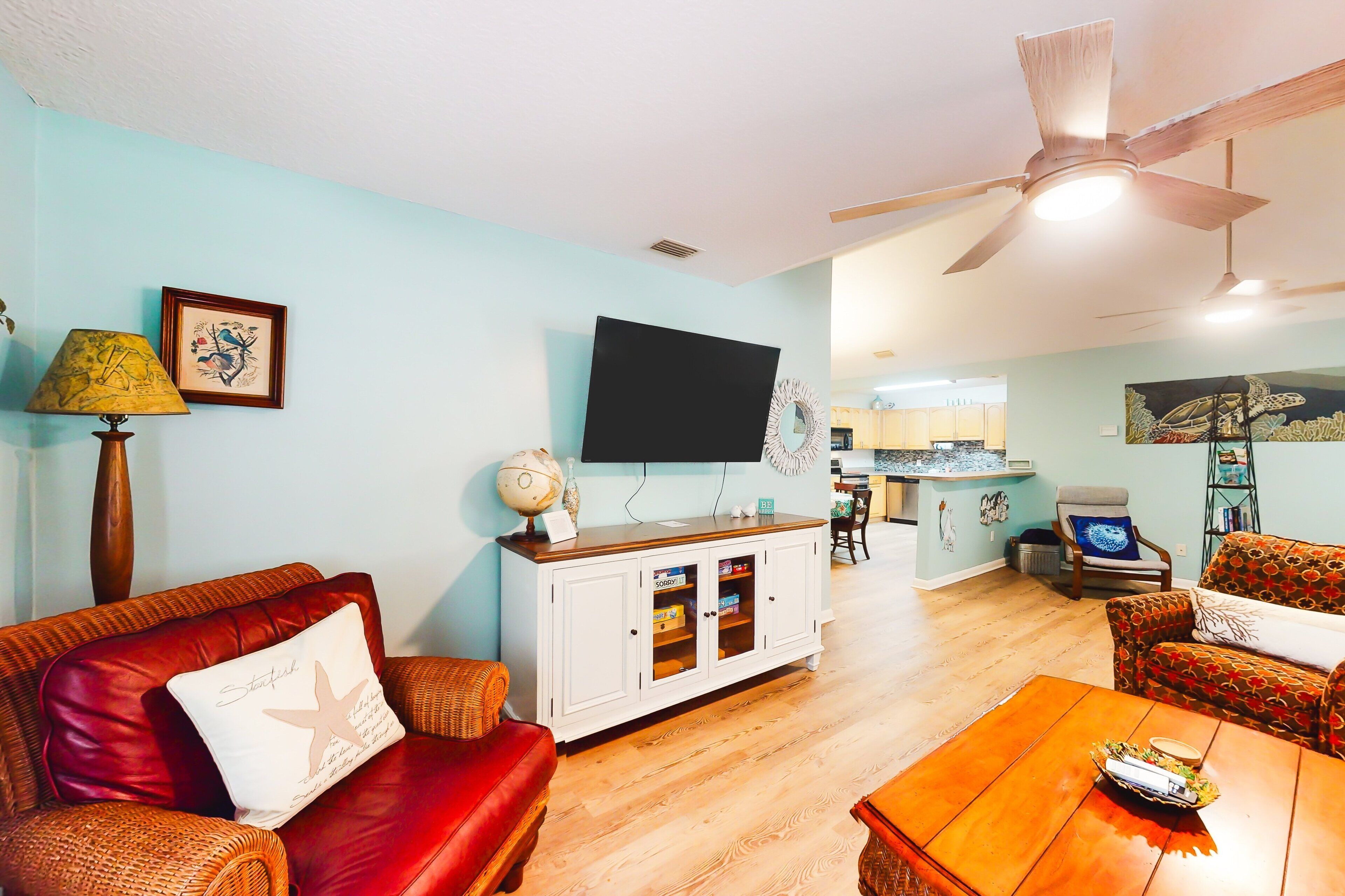 A living room with a red leather sofa, a wooden coffee table, a white cabinet with glass doors, and a flat-screen TV mounted on the wall.