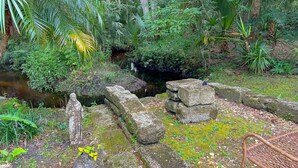 A stone pathway leading through a lush garden with a small stream and a statue. - Serene Home With Enclosed Yard, Grill, Games, & Central AC - Dog-friendly (St. Augustine)