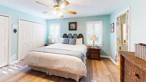 A bedroom with a bed, a ceiling fan, a nightstand, a wicker basket, and a window with curtains. - Serene Home With Enclosed Yard, Grill, Games, & Central AC - Dog-friendly (St. Augustine)