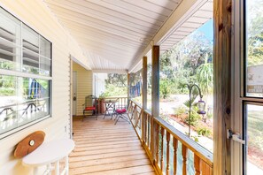 A covered porch with a wooden floor, a table with chairs, and a view of a garden. - Serene Home With Enclosed Yard, Grill, Games, & Central AC - Dog-friendly (St. Augustine)