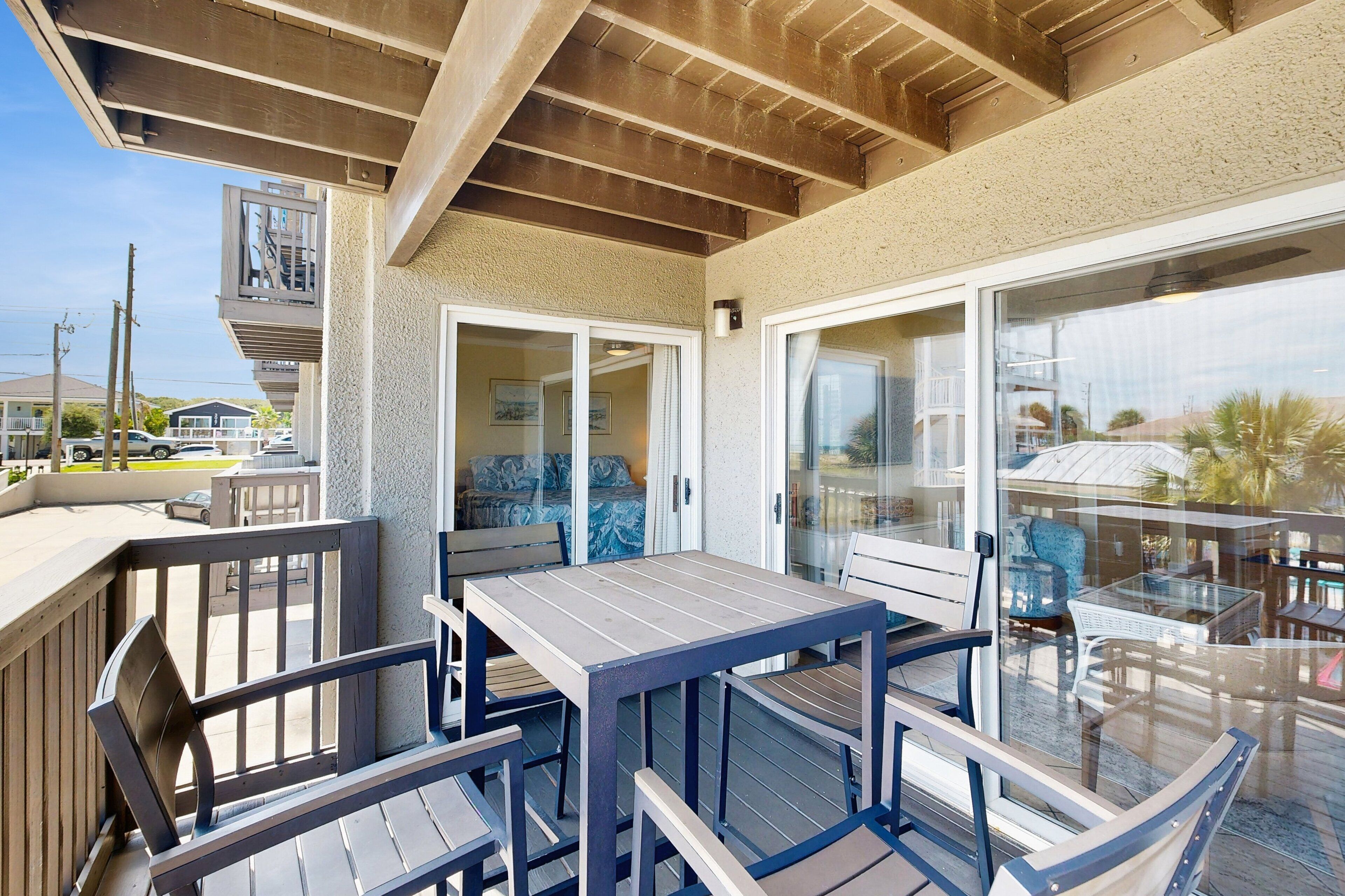 A covered outdoor seating area with a table and chairs, a glass door leading to a room, and a view of the street.