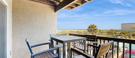 A balcony with a table and chairs, overlooking a beach and a parking area.