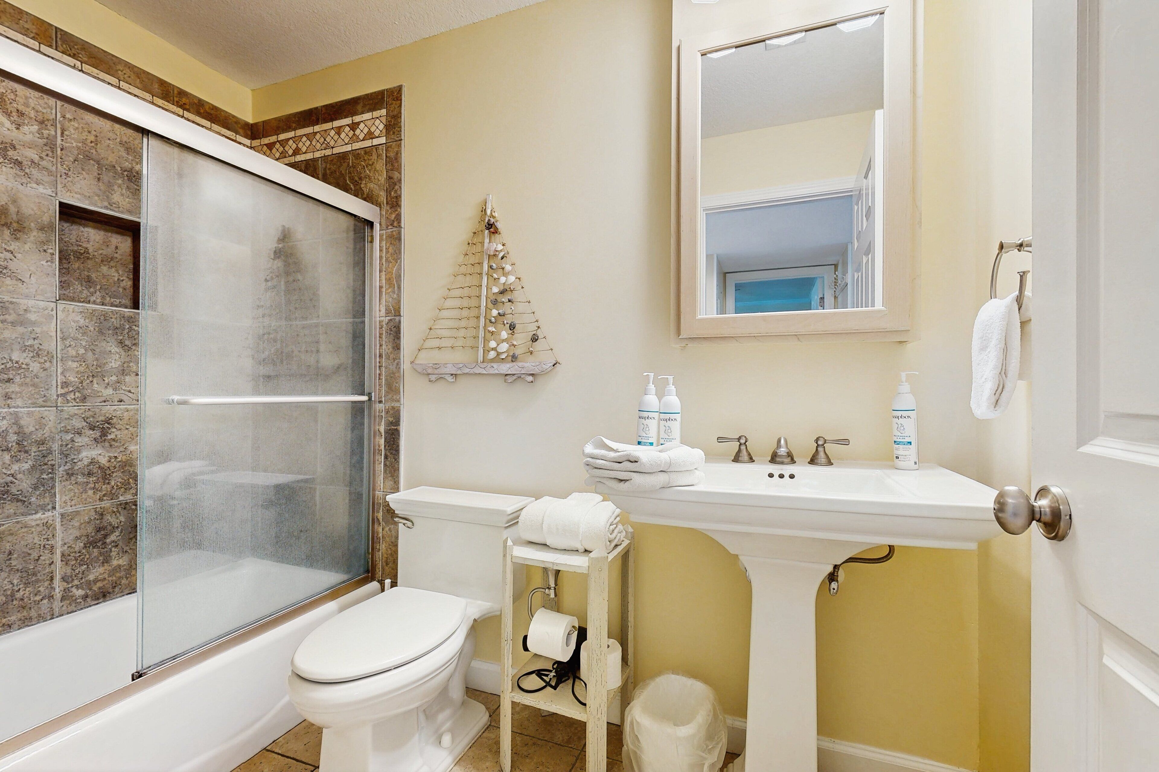 A bathroom with a glass-enclosed shower, a toilet, a sink with toiletries, and a mirror.