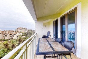 Un balcon avec une table et des chaises, donnant sur un quartier résidentiel avec des maisons et de la verdure.