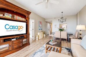 A living room with a television displaying 'Casago Vacation Rentals,' a dining area with a table and chairs, and a ceiling fan. - Seaside Serenity: Beachfront Haven in Palm Coast With Resort Amenities (Palm Coast)