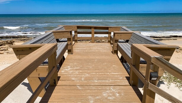 Une promenade en bois mène à des espaces de repos aménagés sur la plage, d’où l’on peut admirer l’océan.