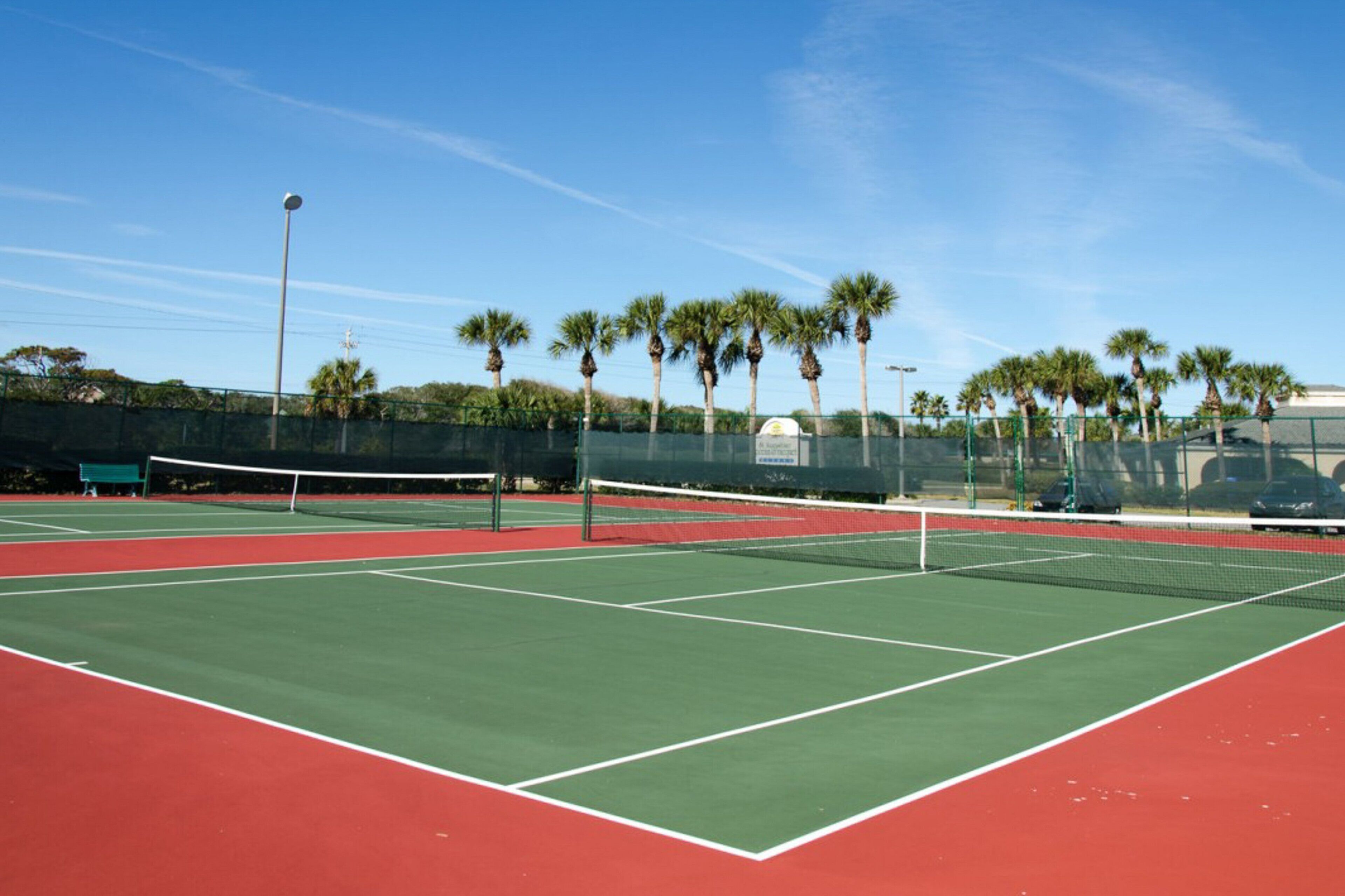 Una cancha de tenis con red, rodeada de palmeras y una valla.