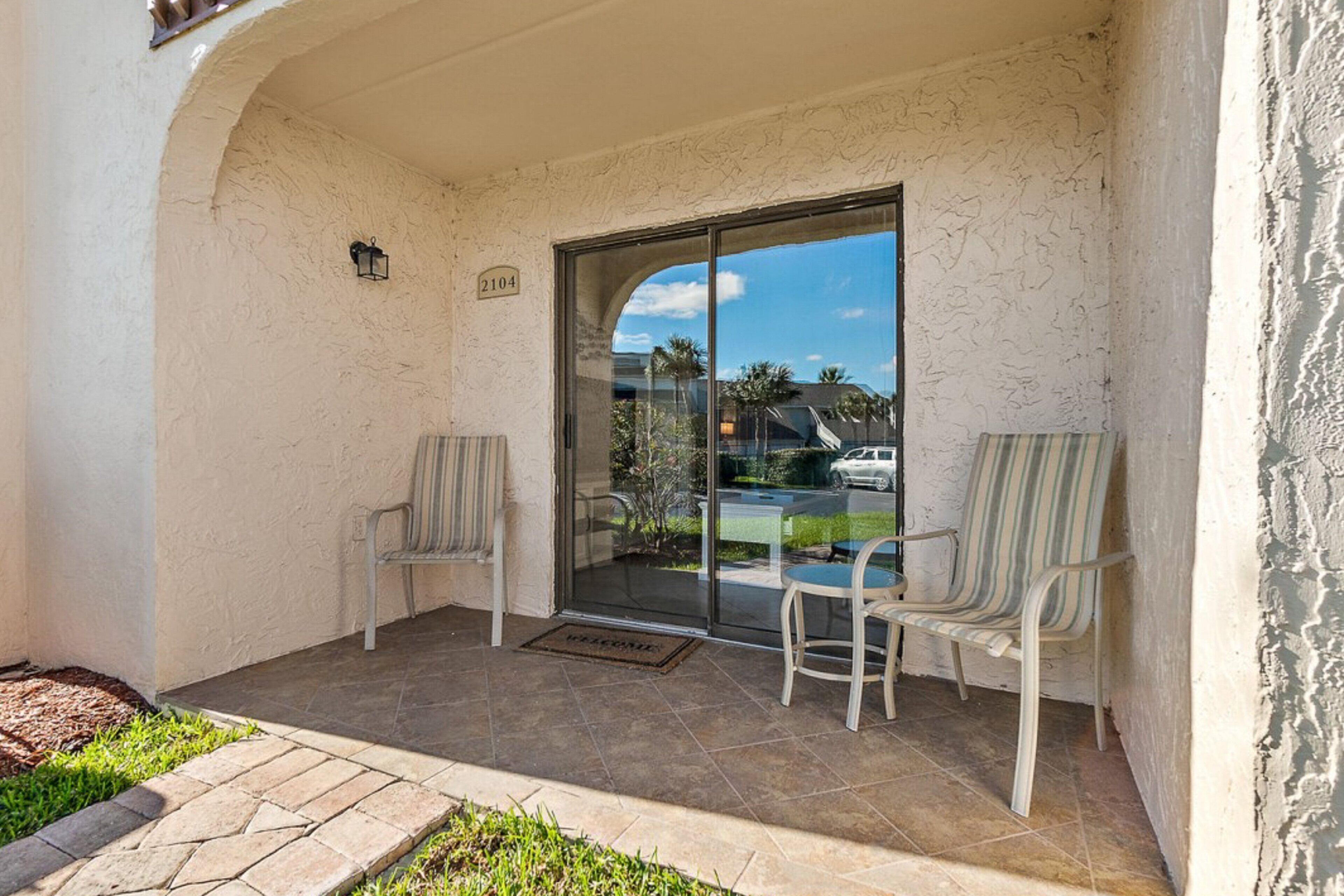 A covered patio with two chairs, a glass door, and a number sign.