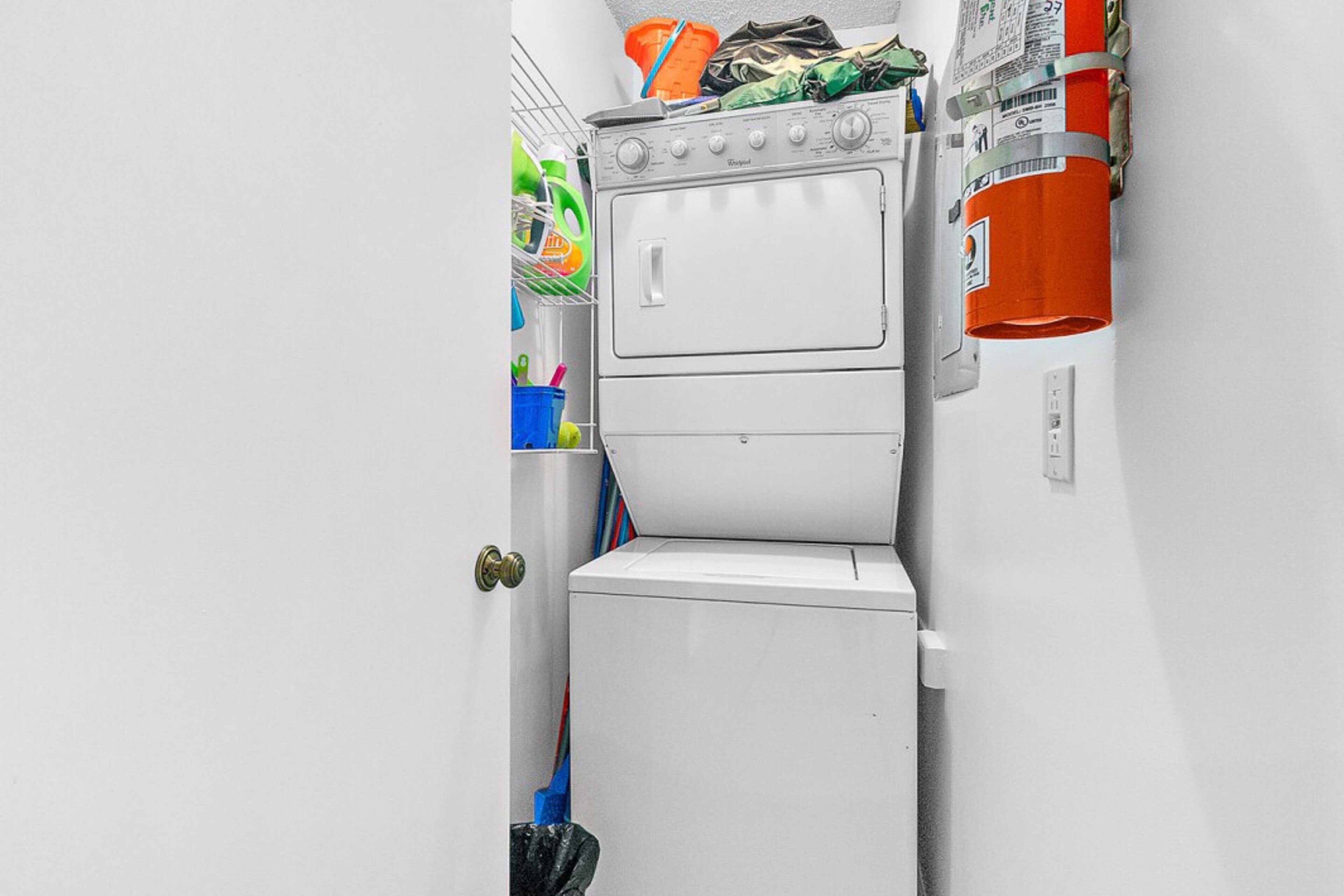 A compact laundry room with a washer and dryer, a small trash bin, and a shelf with cleaning supplies.