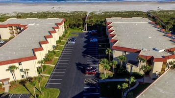 Ein großer Parkplatz mit mehreren Reihen Autos, umgeben von Gebäuden mit roten Dächern und einem Strand im Hintergrund.