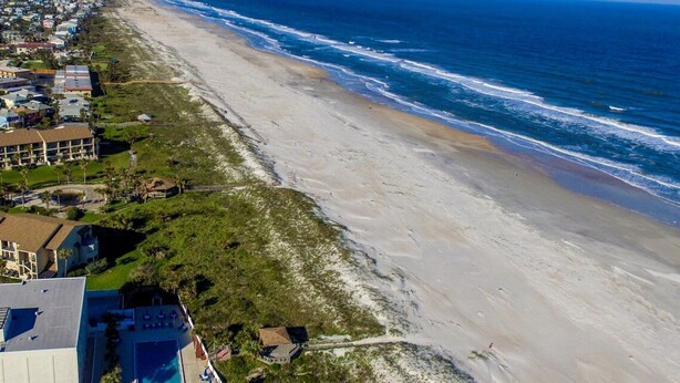 Vue aérienne d’une zone côtière avec une plage, l’océan et des immeubles résidentiels.