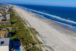 Luftaufnahme einer Küstenregion mit Strand, Meer und Wohnhäusern.