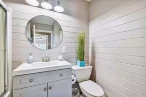 A bathroom with a white vanity, a round mirror, a toilet, and a potted plant. - Spacious Coastal Home in St. Augustine Pool, Outdoor Oasis & Private Suite (St. Augustine)