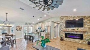 A spacious living area with a dining table, chairs, a coffee table with a plant, a fireplace, and a kitchen in the background. - Spacious Coastal Home in St. Augustine Pool, Outdoor Oasis & Private Suite (St. Augustine)