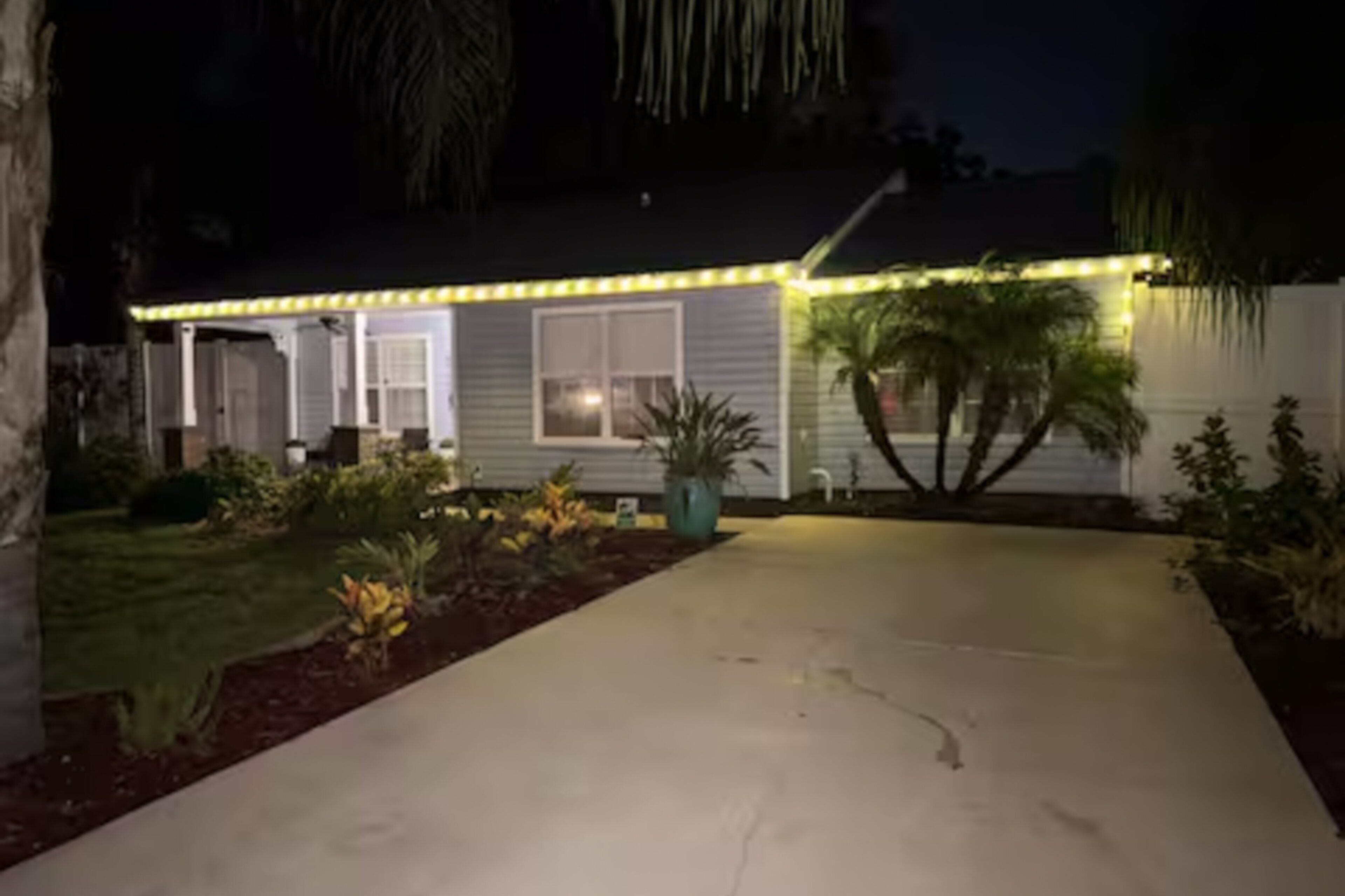 A house with a concrete driveway, a front porch, and a well-lit exterior.