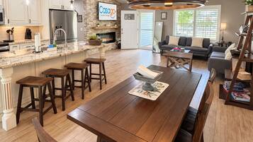 A spacious kitchen with a central island, a dining area with a long table, and a living room with a sofa and a fireplace.