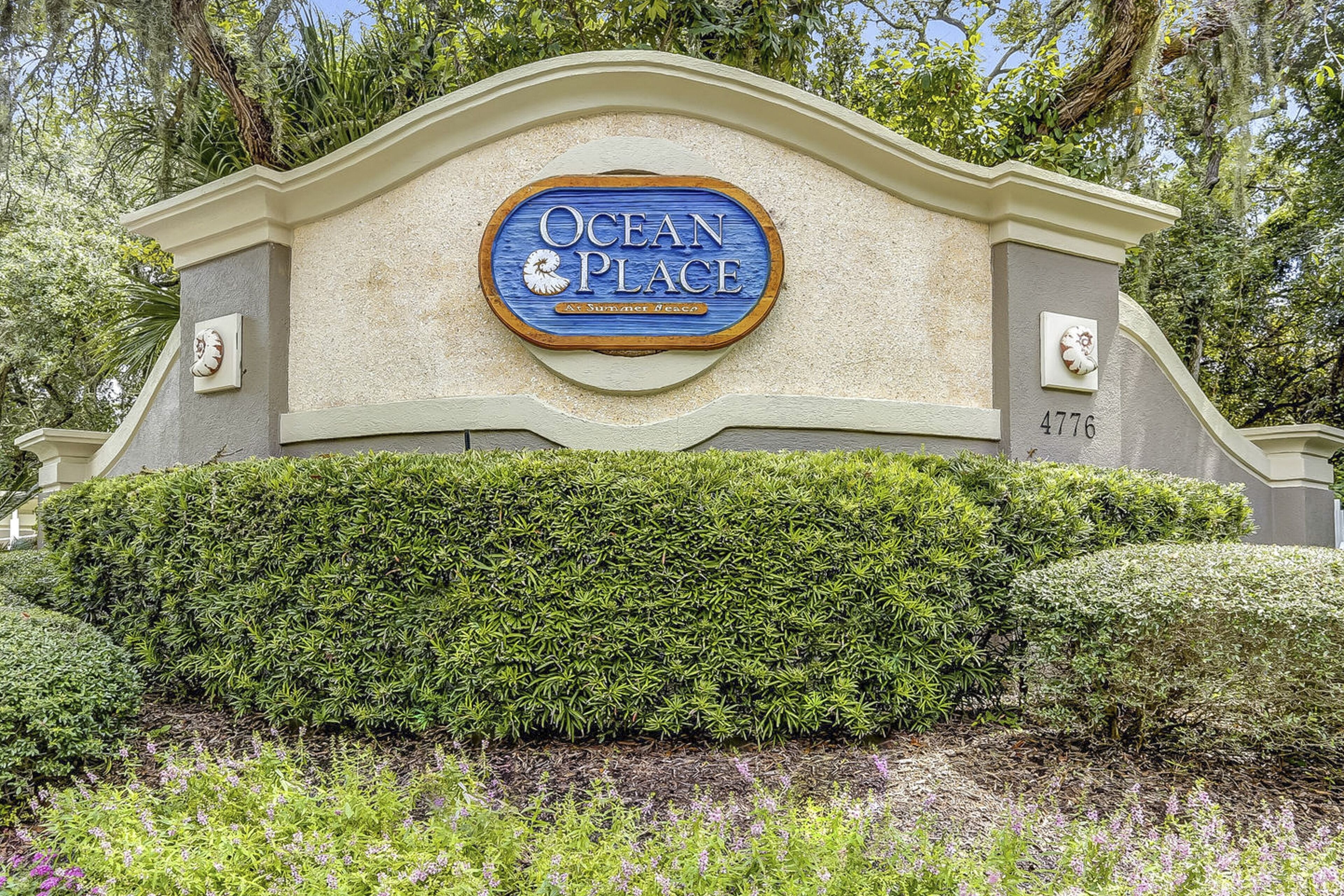 A sign for Ocean Place, a resort-style hotel with a landscaped entrance and a well-maintained hedge.