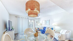 A modern living room with a glass dining table surrounded by wicker chairs, a blue sofa, and a striped armchair. - Recently Updated Resort Condo With 2 Pools, 2 Balconies, Ocean Views, Bbq, & W/D (St. Augustine)