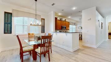 A modern kitchen with wooden cabinets, a glass island, and a dining area with a glass table and wooden chairs.