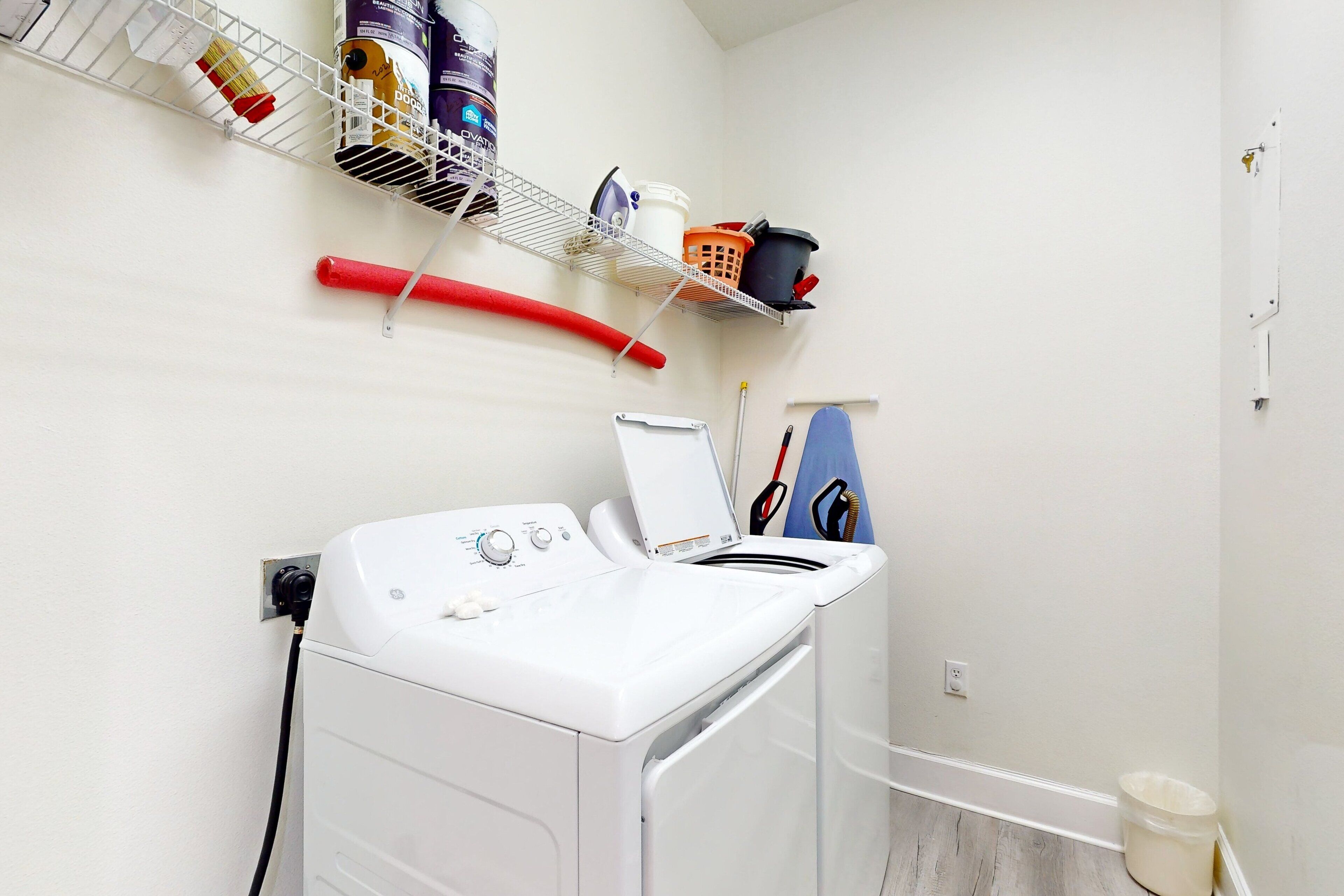 Un espace dédié à la lessive, comprenant un lave-linge, une étagère avec des produits de nettoyage et un balai-serpillière.