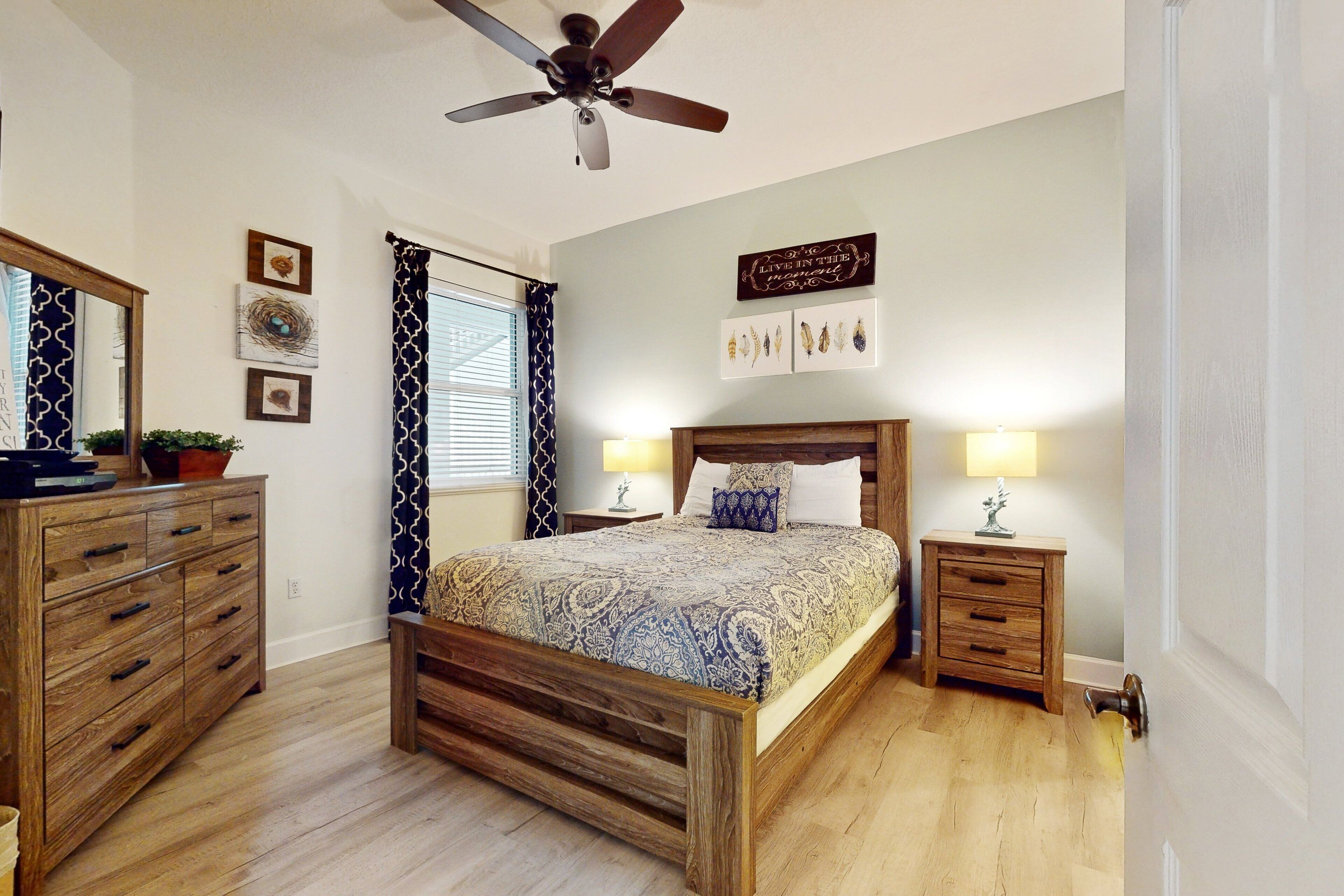 Une chambre à coucher avec un lit en bois, un ventilateur de plafond, une commode et une table de chevet avec une lampe.