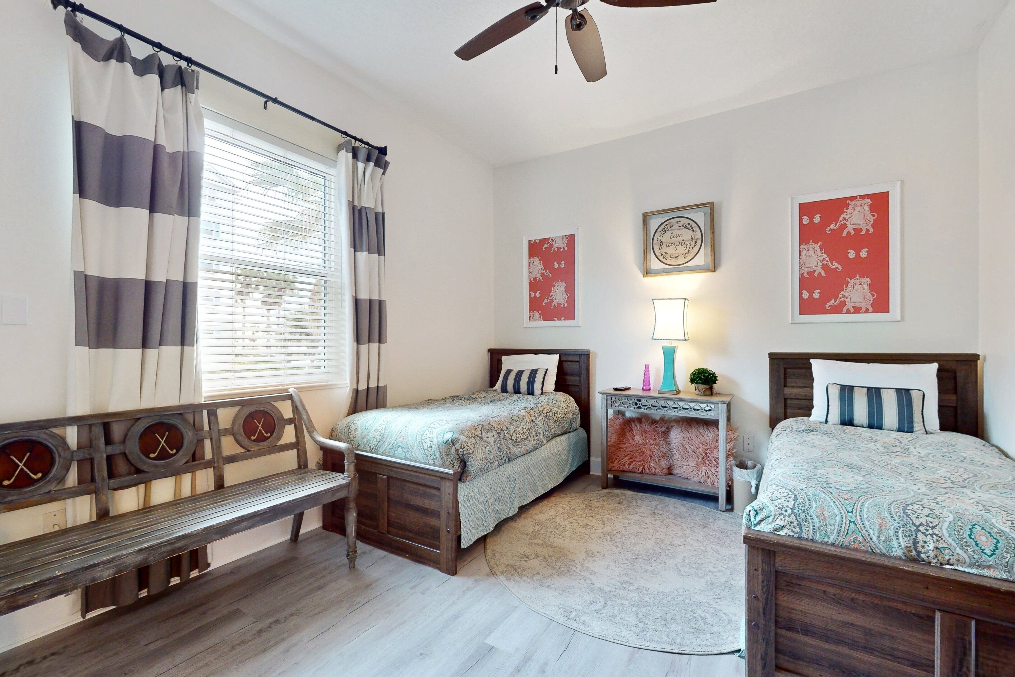 A bedroom with two beds, a bench, a nightstand, and a ceiling fan.