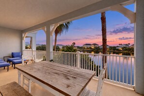 A covered outdoor area with a wooden table and blue chairs, overlooking a body of water and houses. - Second Floor, Dog-friendly Condo With Shared Pool, High-speed Wifi, & Central AC (Palm Coast)