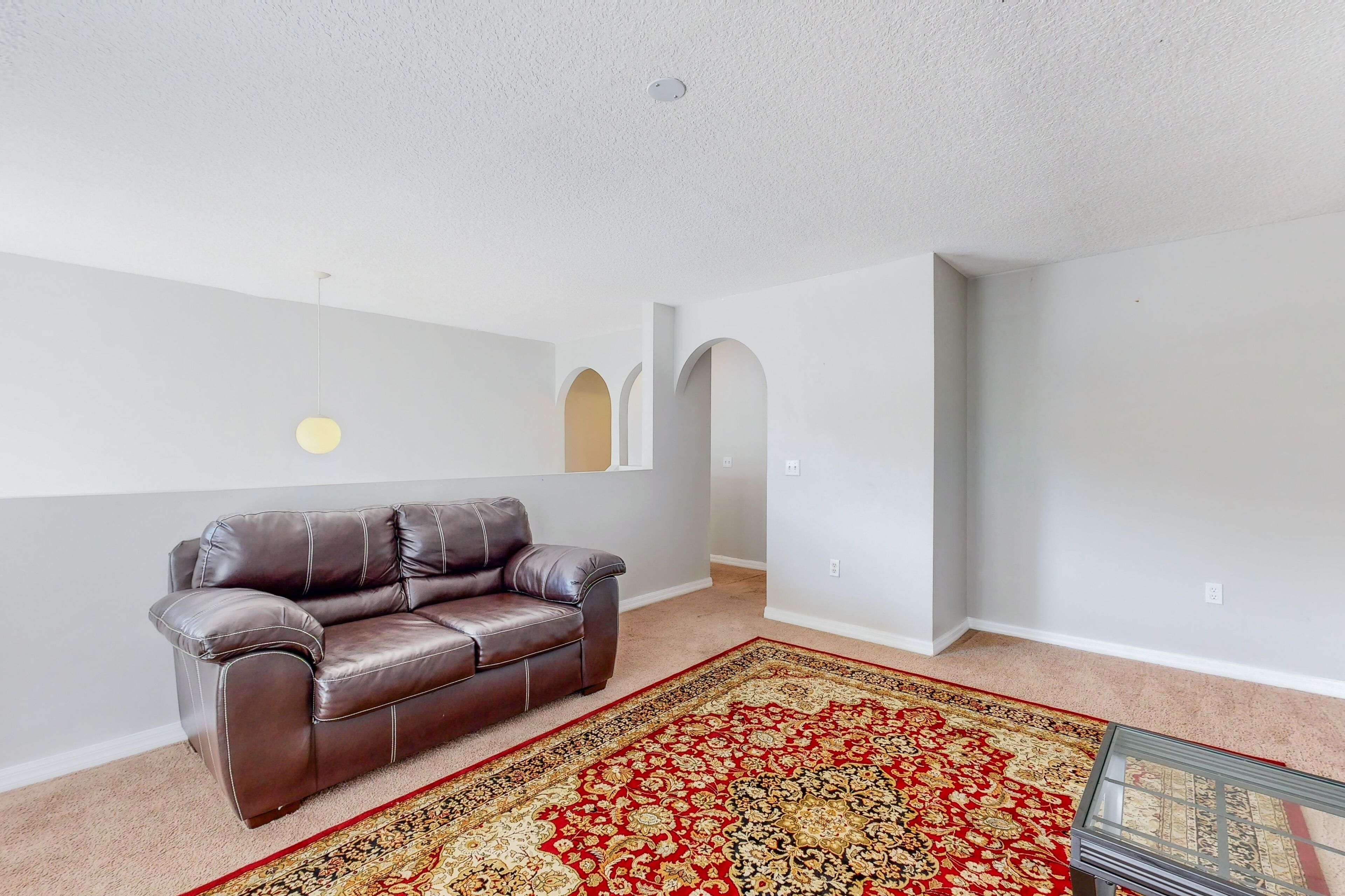 A living room with a brown leather sofa, a patterned rug, and a glass coffee table.