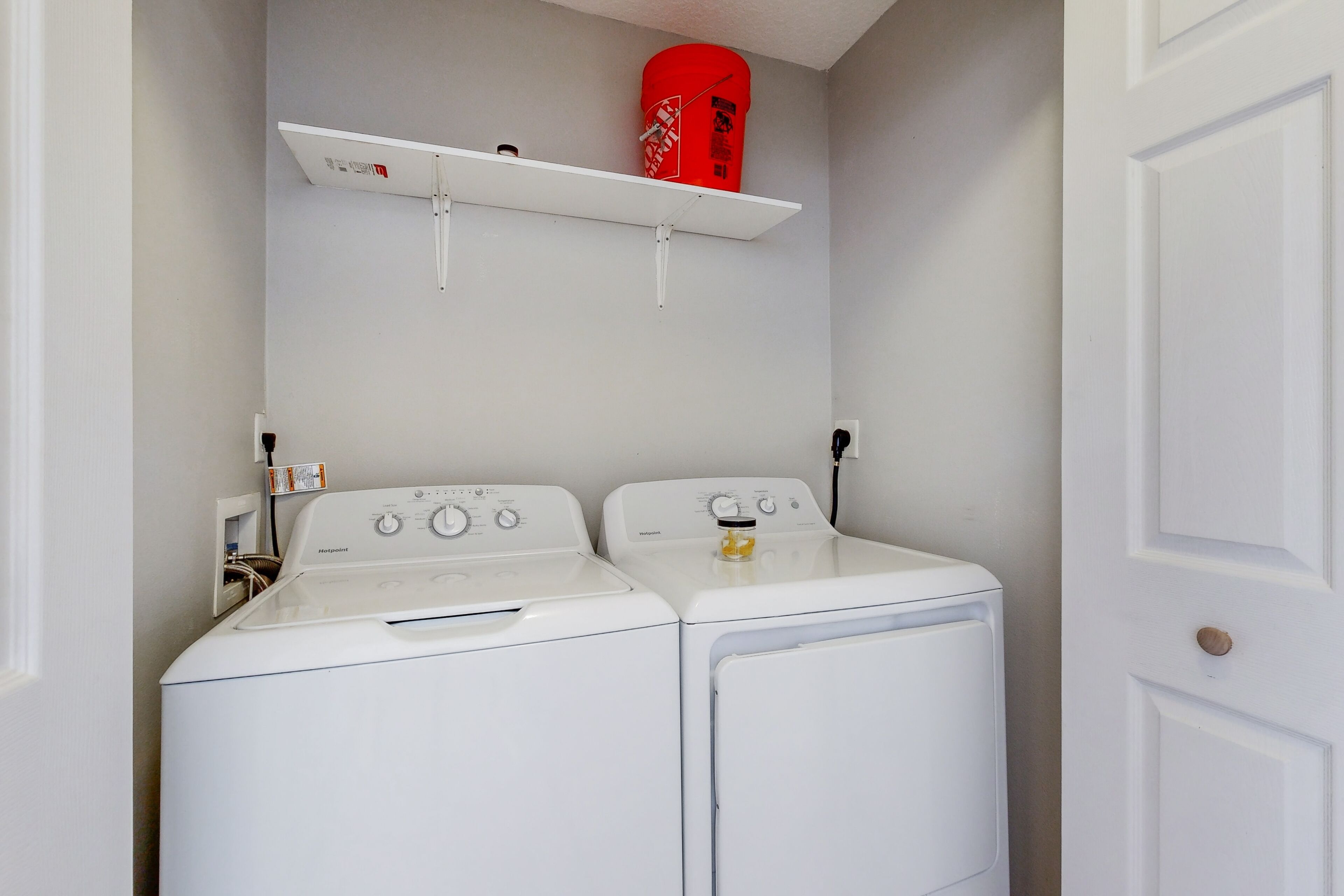 A laundry room with two white front-loading washing machines and a red fire extinguisher on a shelf above them.