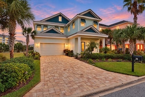 A two-story house with a garage, surrounded by well-maintained landscaping and palm trees. - Palm-surrounded Stunner With Enclosed Pool & Water Views - Dog-friendly (Palm Coast)