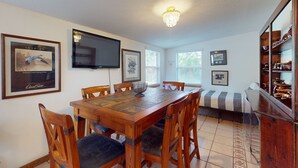 A dining area with a wooden table, chairs, a TV, framed pictures, and a bookshelf. - Spacious Pet -friendly Home w/ Fenced in Yard and Close to The Beach (St. Augustine)