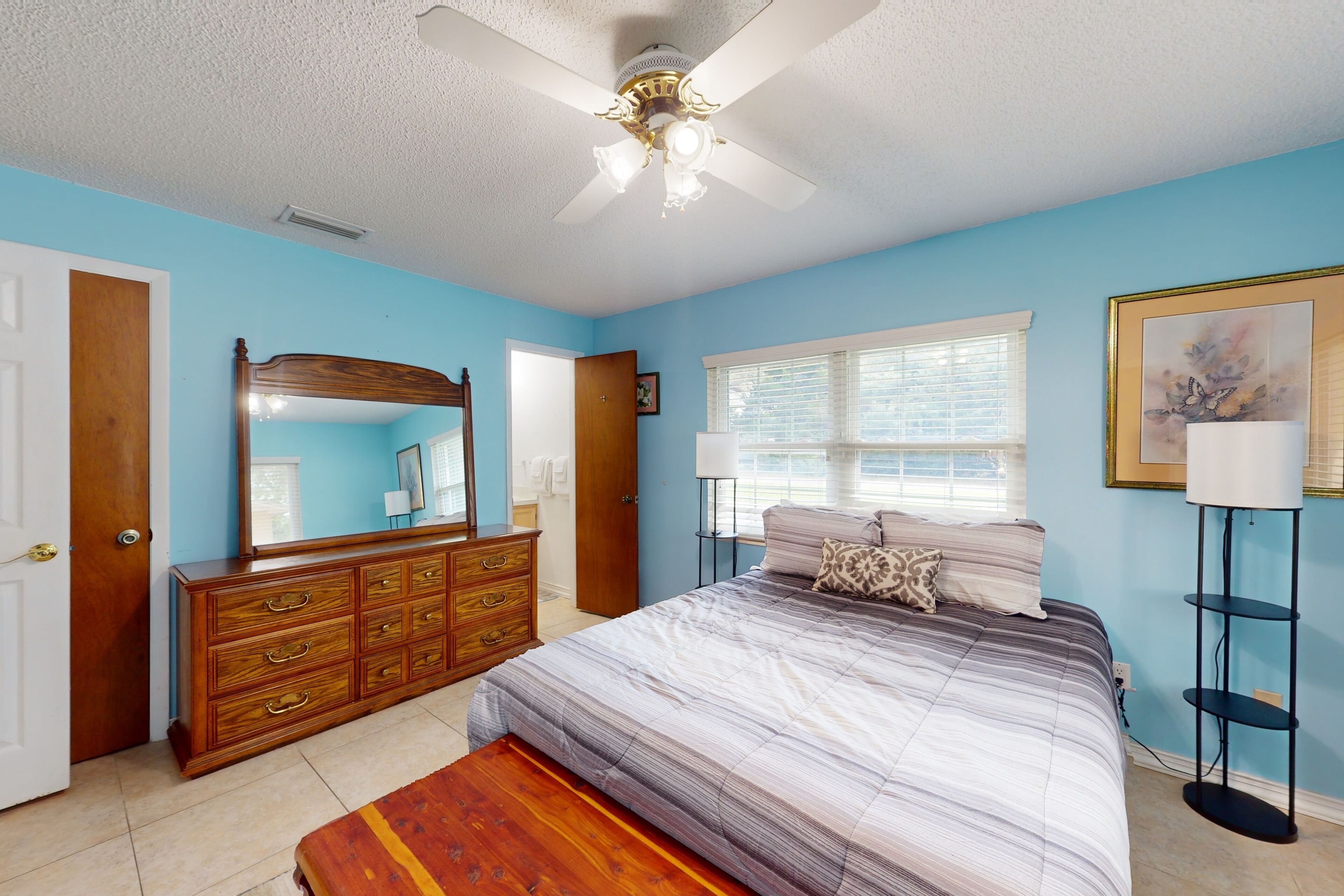 A bedroom with a bed, dresser, mirror, window, and ceiling fan.