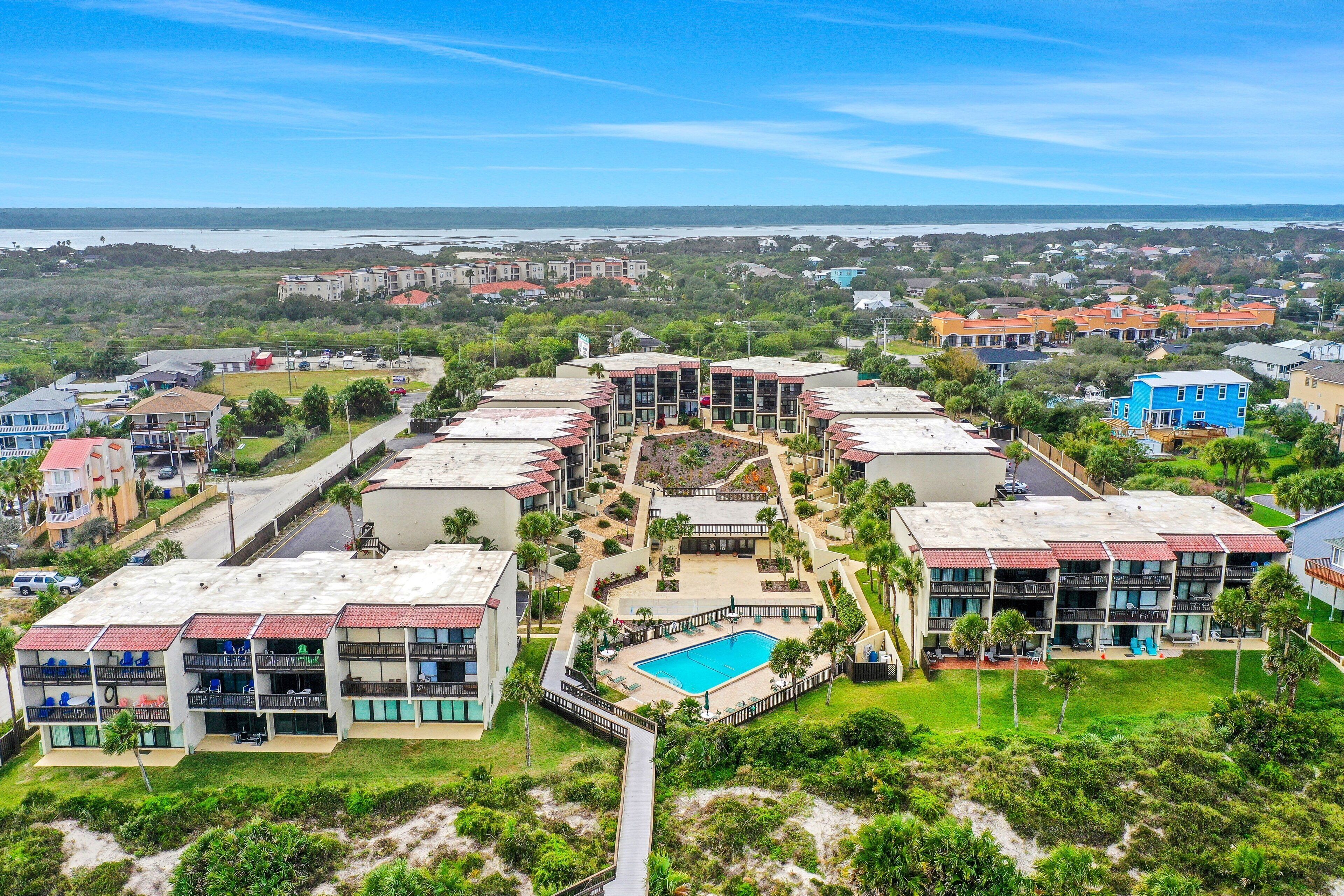 A resort with multiple buildings, a central pool, and a view of the ocean.