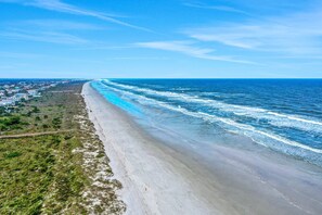 A coastal beach with a long stretch of sandy shore, a road parallel to the beach, and a distant view of a town. - Oceanview Condo With Beach Access, Pool, Tennis Courts and Private Patio (St. Augustine)