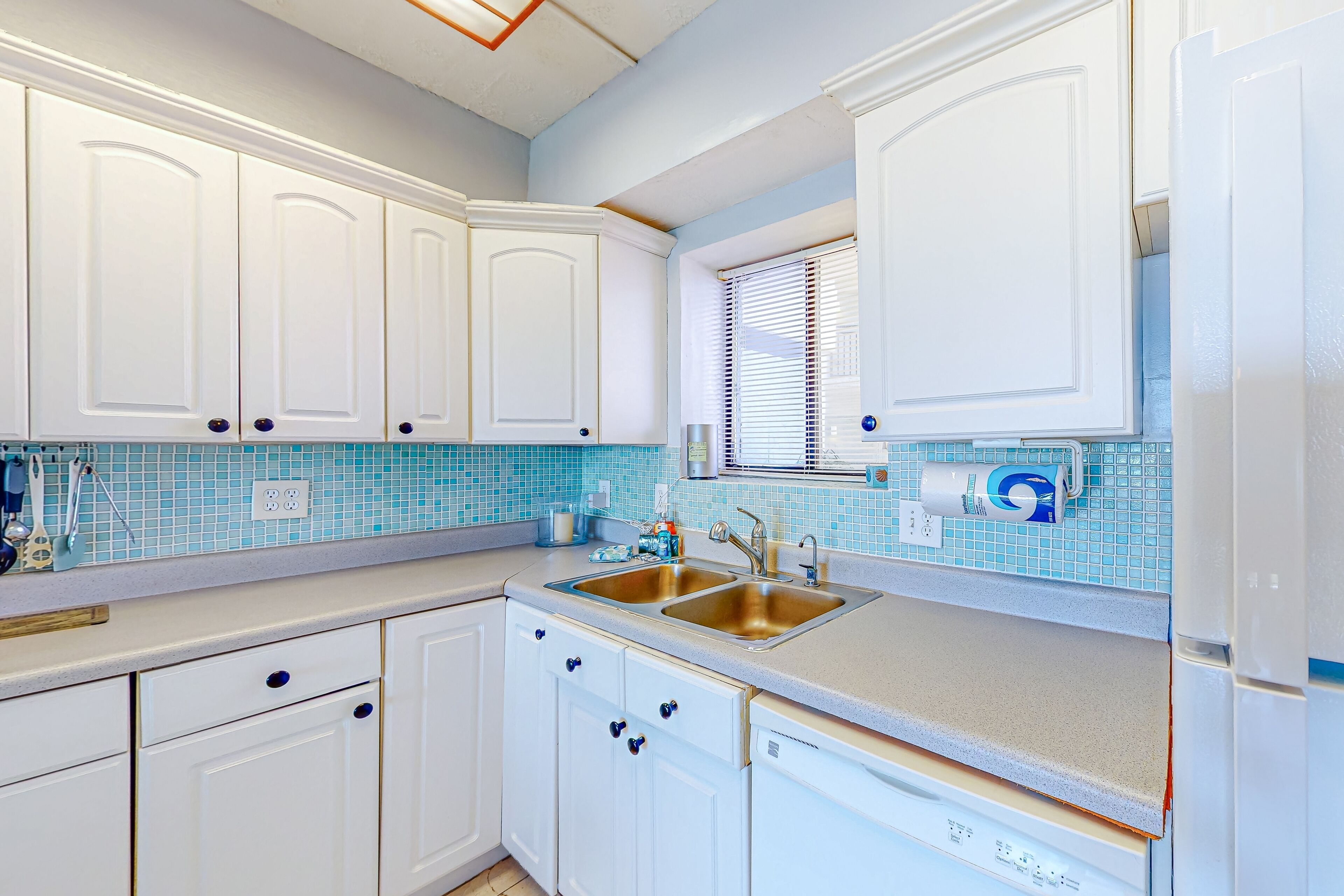A kitchen with white cabinets, a double sink, and a window with blinds.