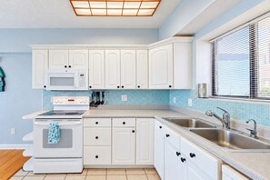 A kitchen with white cabinets, a microwave, a stove, and a window with blinds. - Oceanview Condo With Pool, Beach Access, Jetted Tub, W/d, & AC (Jacksonville Beach)