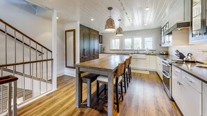 A modern kitchen with a wooden island, white cabinets, and a staircase with a metal railing. - Oceanfront Townhouse With Ocean Views, Central AC, Wifi, & Outdoor Pool (Fernandina Beach)