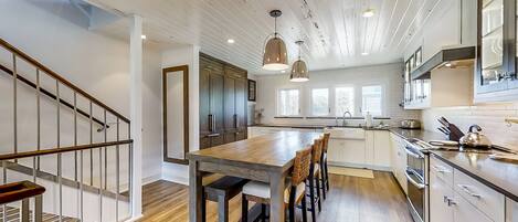 A modern kitchen with a wooden island, white cabinets, and a staircase with a metal railing.