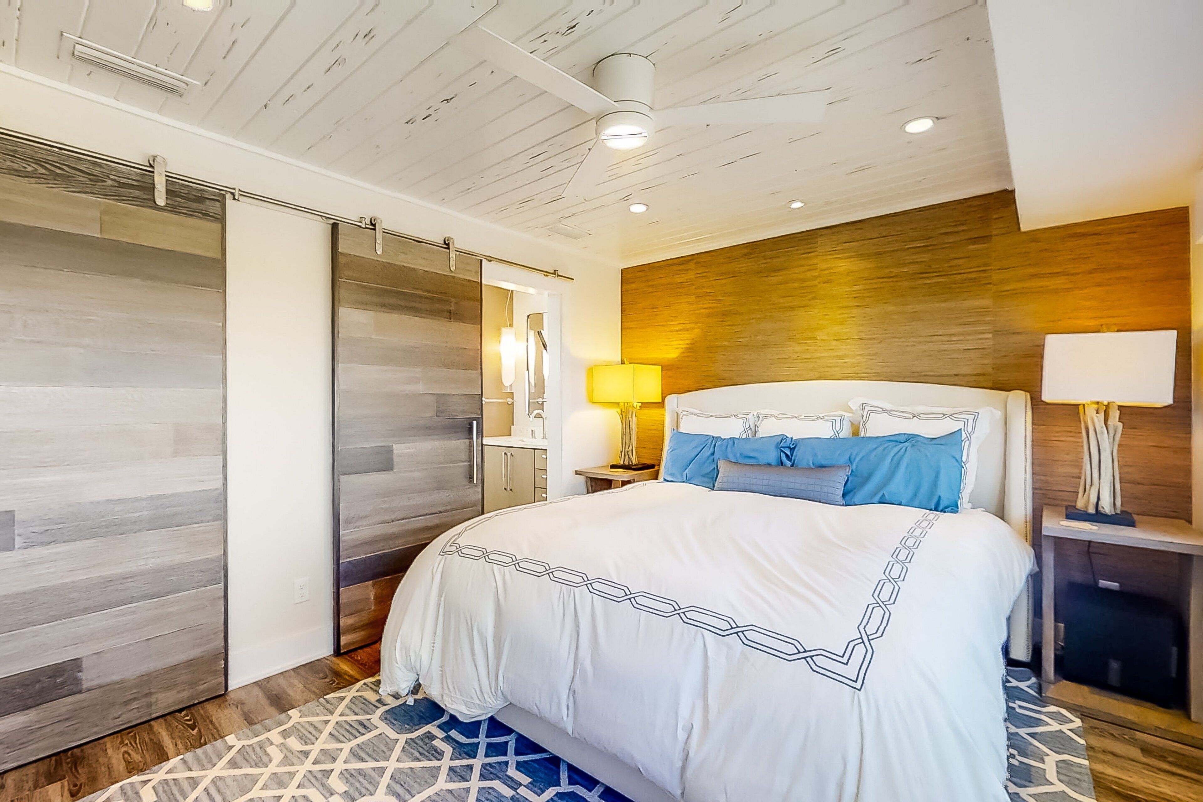 Ein modernes Hotelzimmer mit einem großen Bett, Wandverkleidung aus Holz und einem Teppich mit geometrischem Muster.